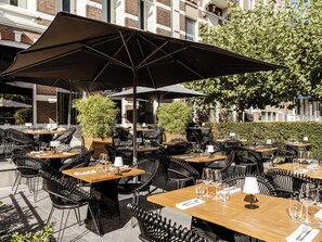 An outdoor dining area with multiple tables and chairs, umbrellas, and potted plants. - Boutique Hotels MANNA & Blue (Nijmegen)