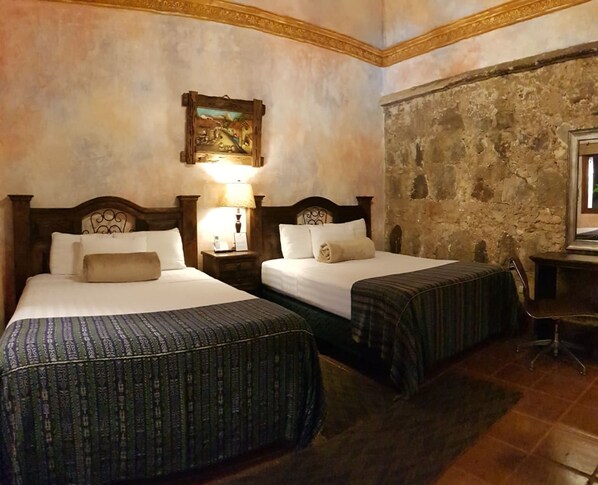 Una habitación con dos camas, cada una con cabecero y mesita de noche con lámpara. Un cuadro cuelga de la pared sobre las camas.