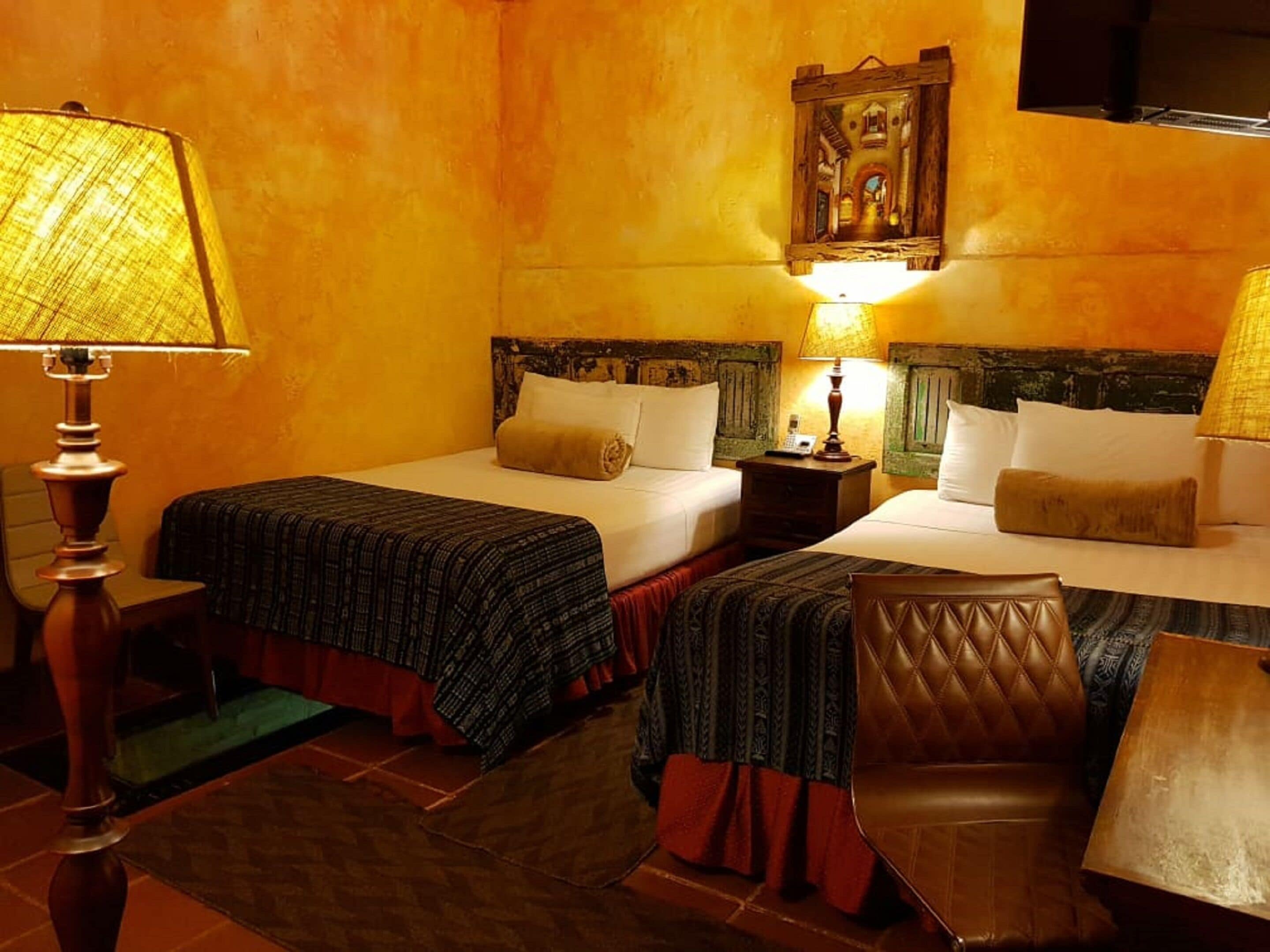 Une chambre d’hôtel avec deux lits, chacun doté d’une tête de lit en bois, d’une petite table de chevet et d’une lampe.