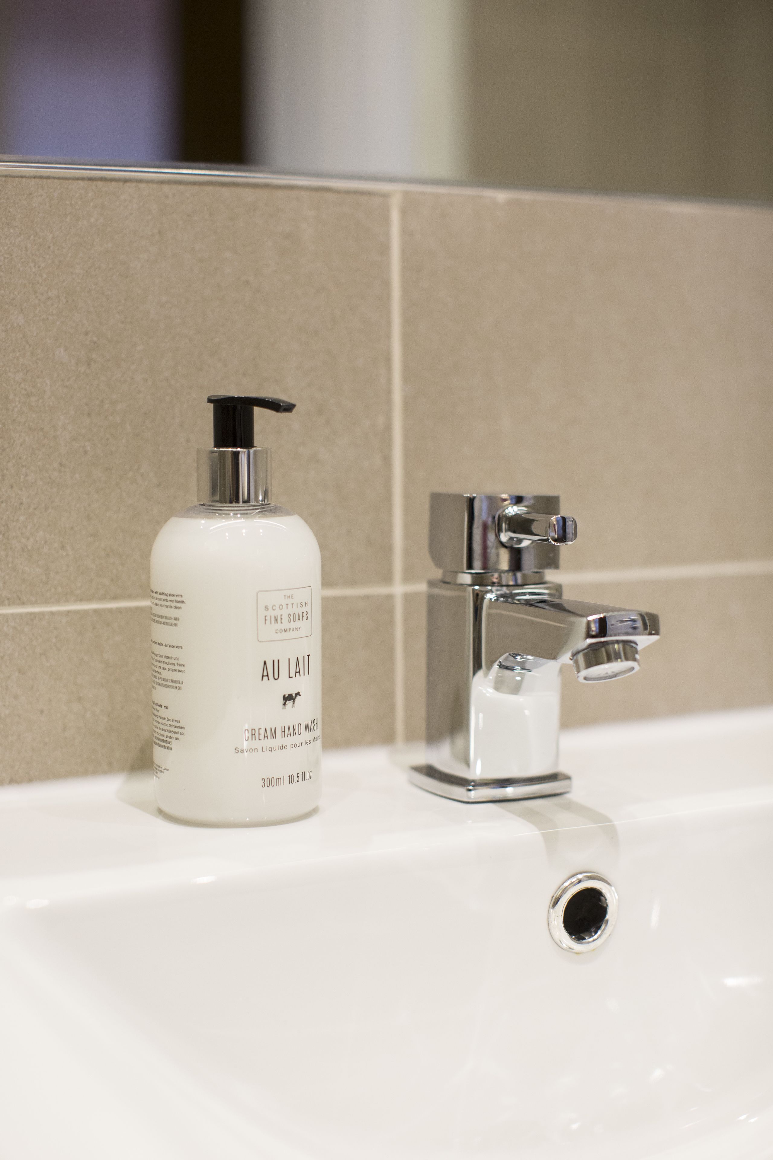 A bathroom sink with a bottle of hand soap and a chrome faucet.