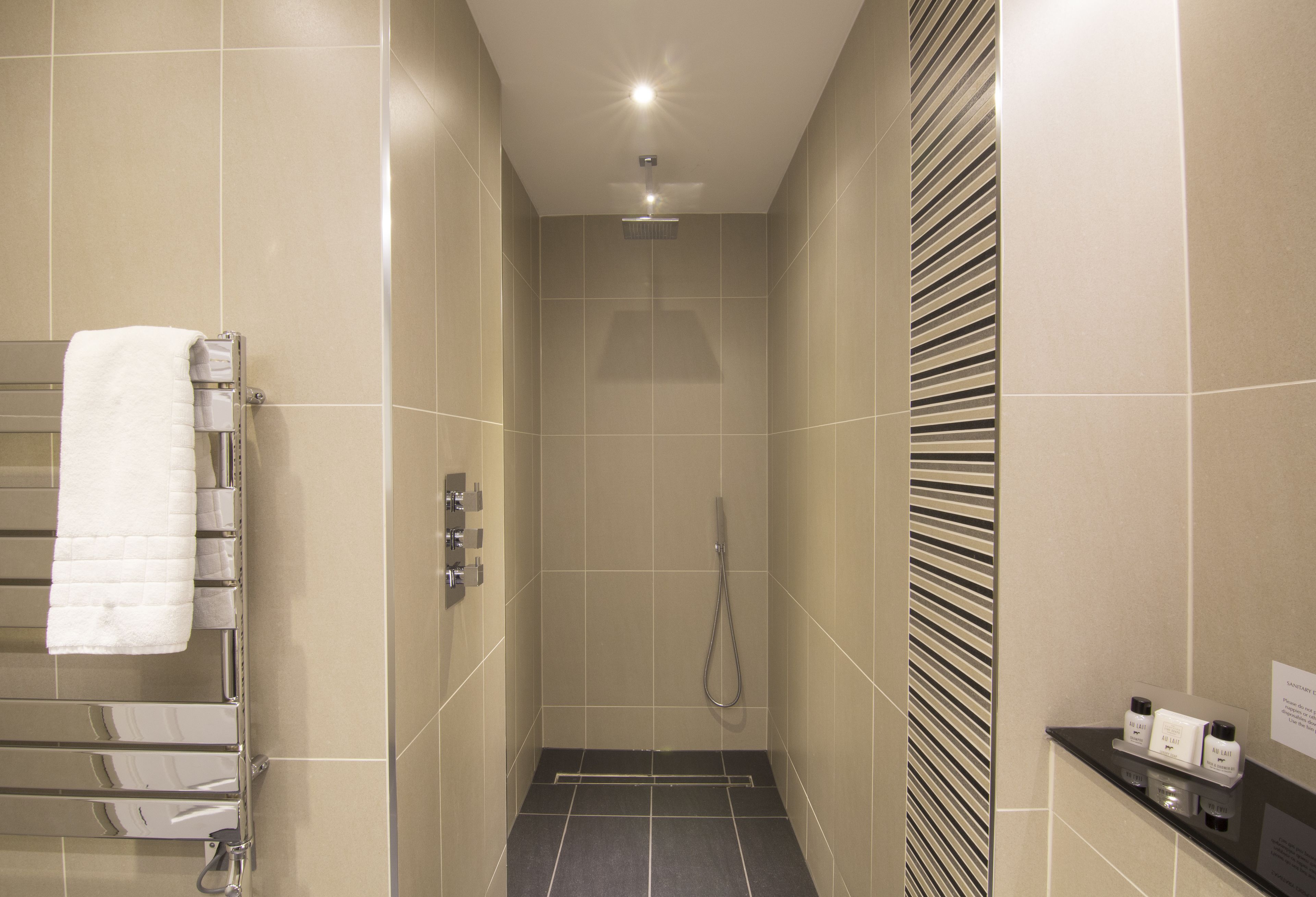 A modern bathroom with a shower, a towel rack, and a small shelf with toiletries.