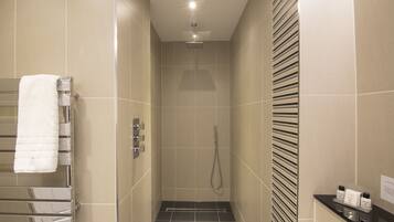 A modern bathroom with a shower, a towel rack, and a small shelf with toiletries.