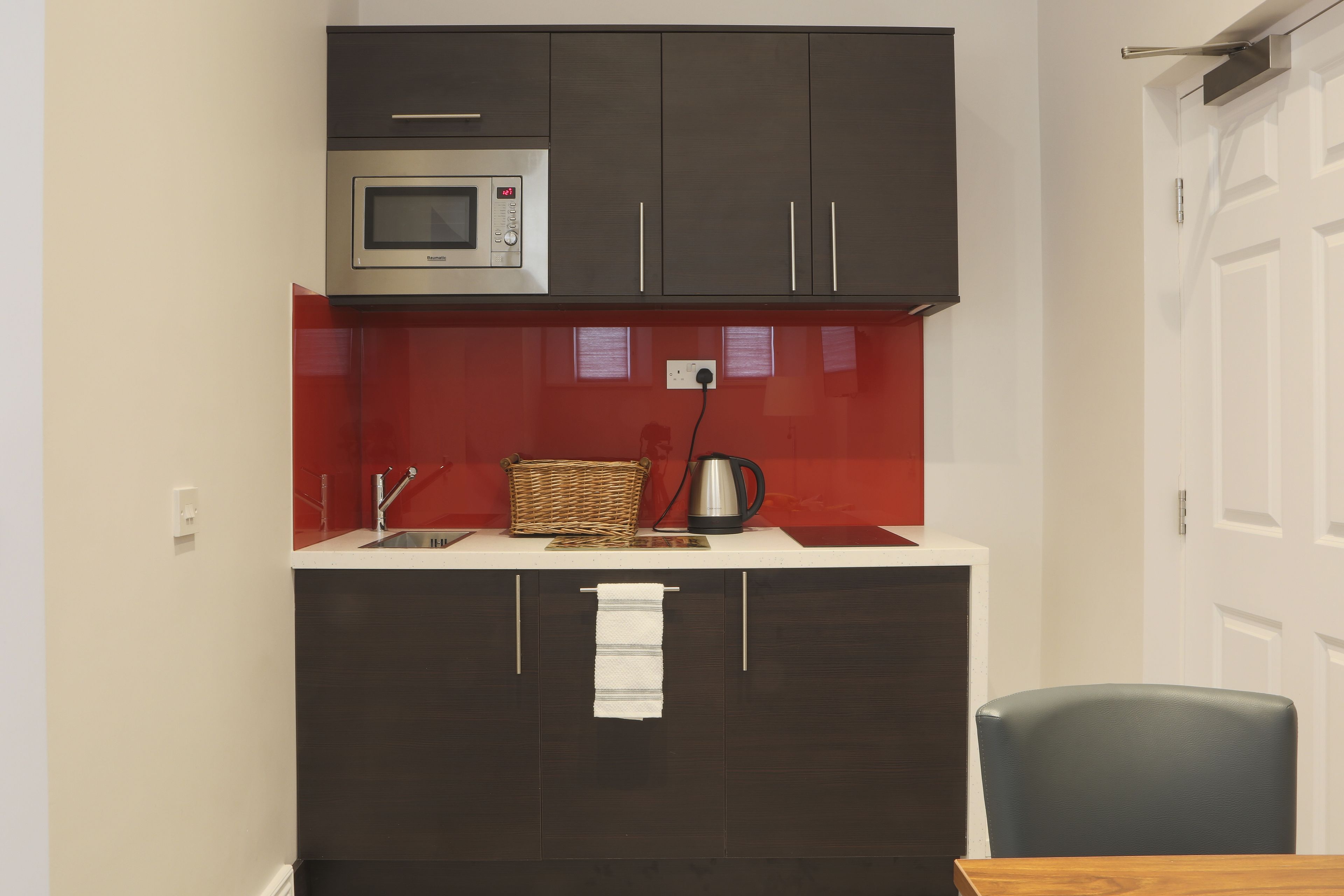 A compact kitchen with dark cabinets, a microwave, a sink, and a small table.
