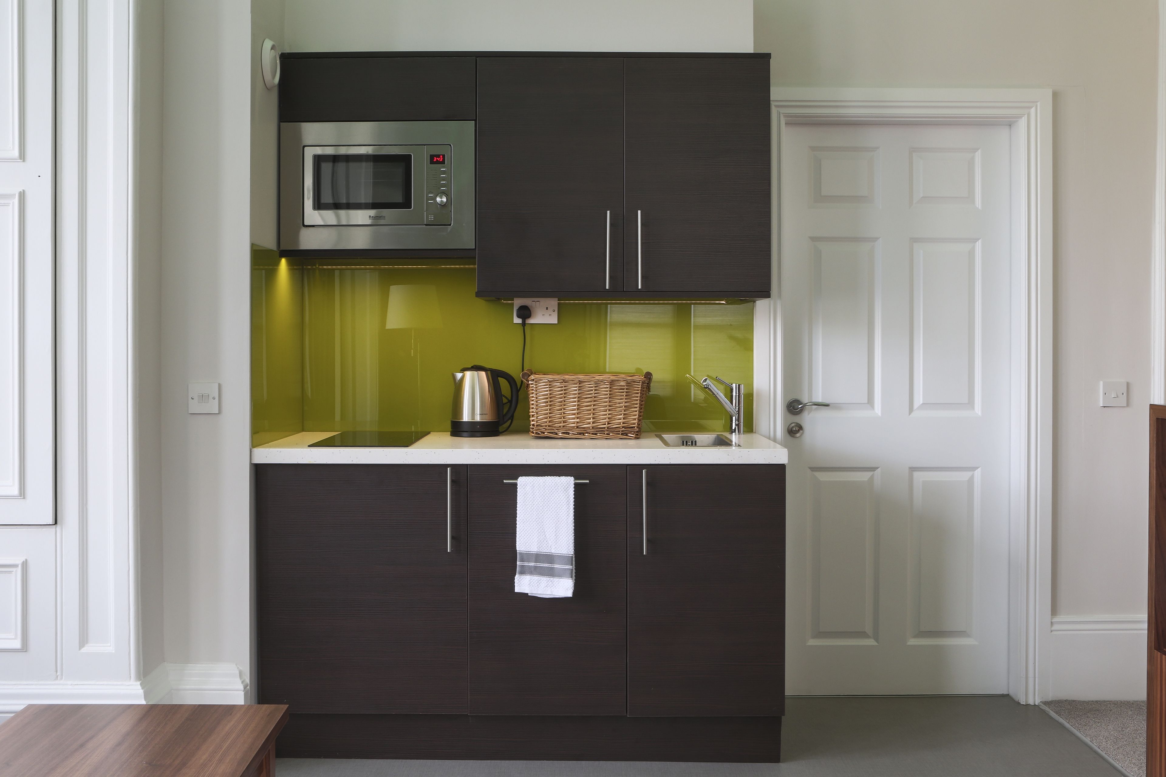 A compact kitchen with dark cabinets, a microwave, a sink, and a wicker basket.