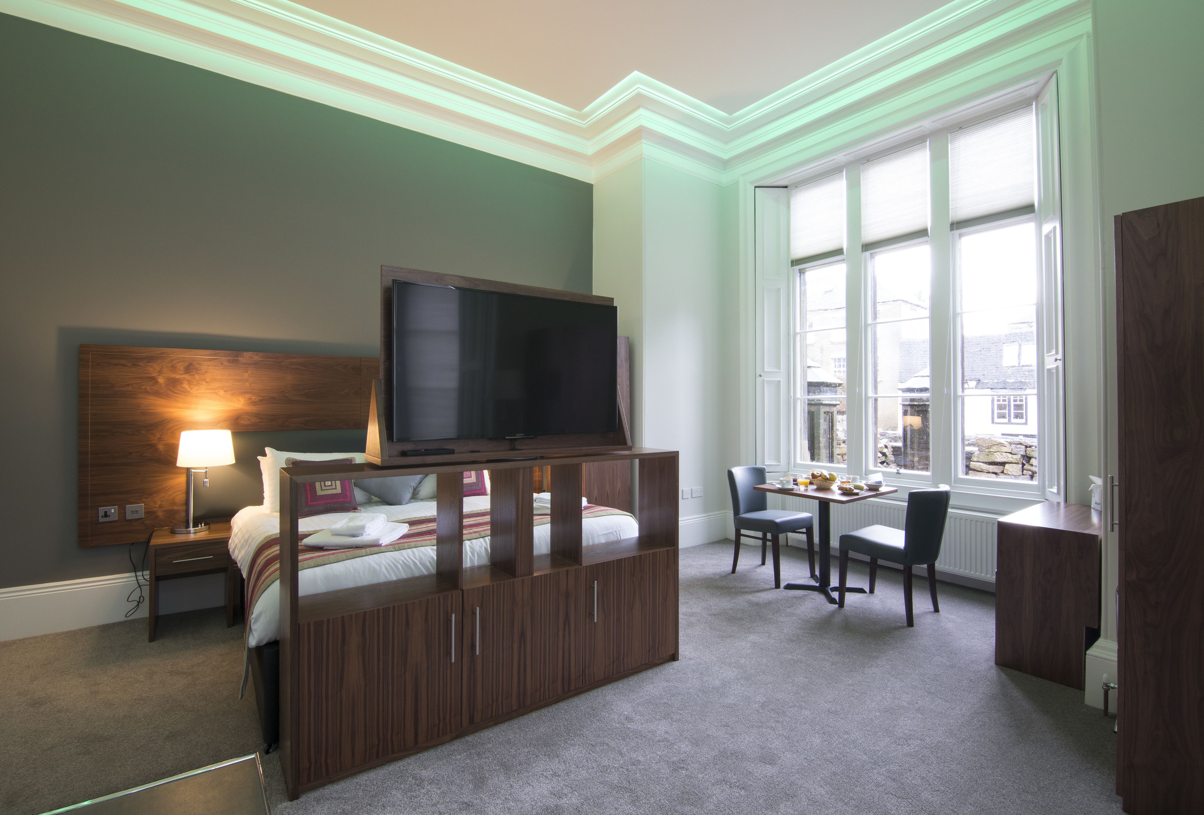 A hotel room with a bed, a TV, a desk, and a window with a view of buildings.