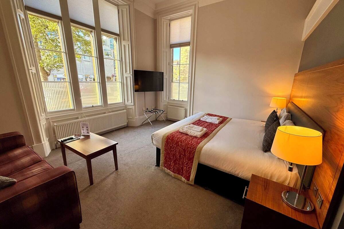 Une chambre d’hôtel équipée d’un lit, d’une télévision, d’un bureau, d’une chaise et de grandes fenêtres.