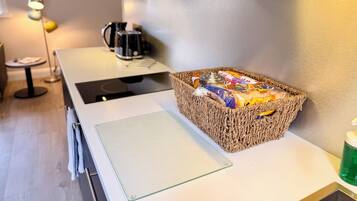 A kitchen with a coffee maker, a basket of snacks, a cutting board, and a green bottle.