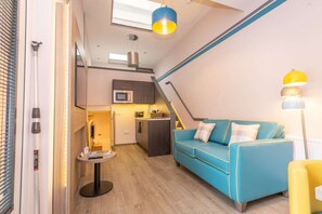 A compact living space with a kitchenette, a blue sofa, and a small dining table.