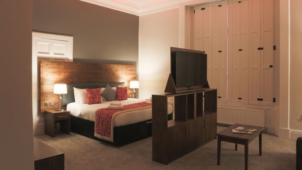 A hotel room with a bed, bedside tables, a TV, a cabinet, and a radiator. - Court Residence (Linlithgow)