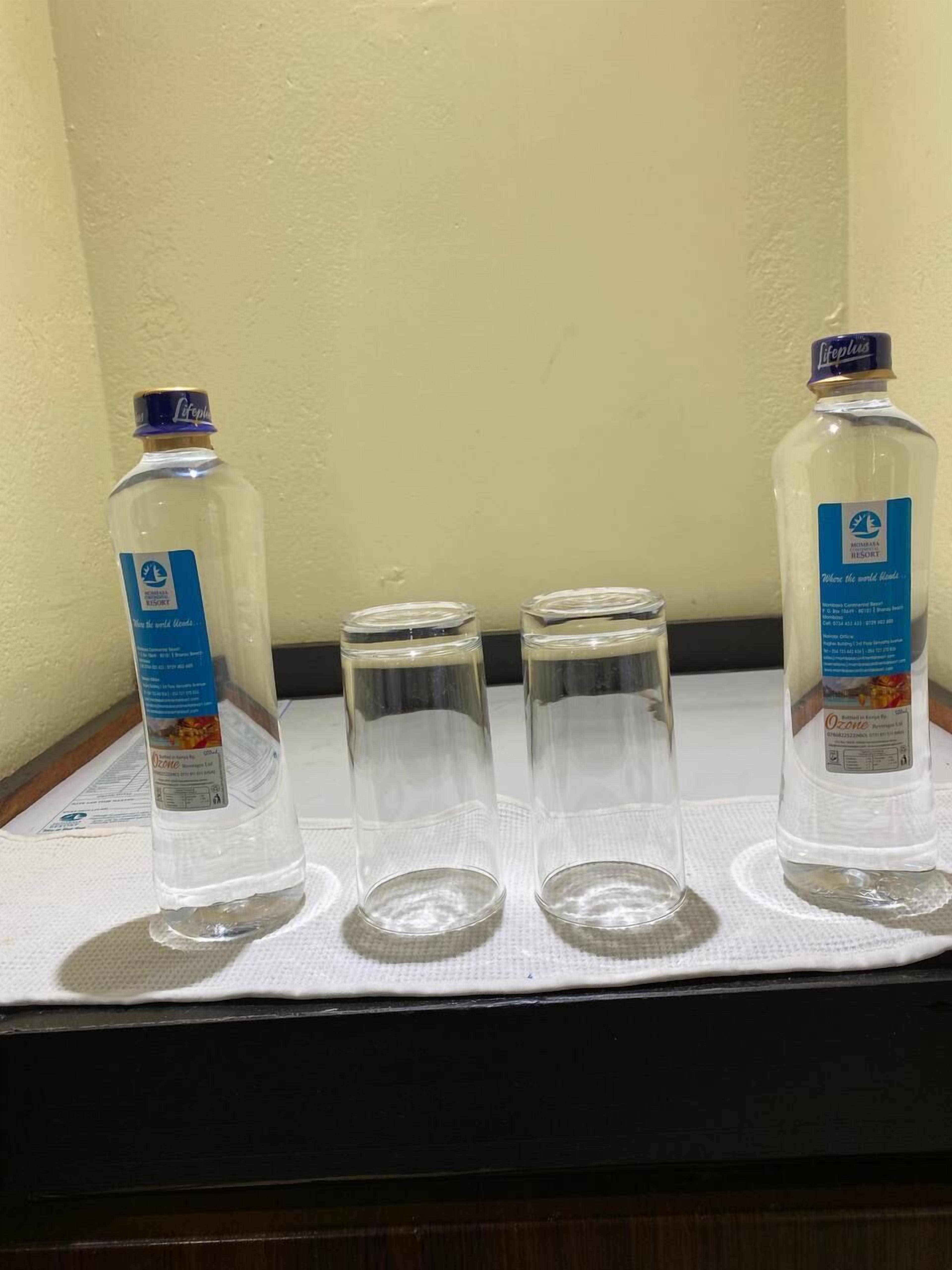 Two bottles of Ozone water and three empty glasses on a table.