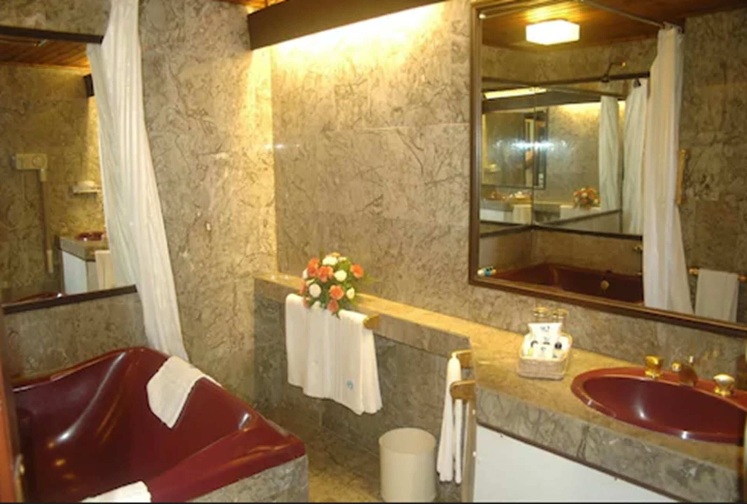 A bathroom with a marble wall, a red sink, a mirror, and a shower curtain.