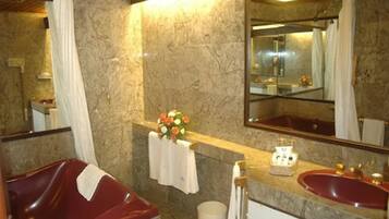 A bathroom with a marble wall, a red sink, a mirror, and a shower curtain.