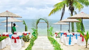 A beach wedding aisle with white chairs, red and blue sashes, and thatched umbrellas. - Mombasa Continental Resort (Mombasa)