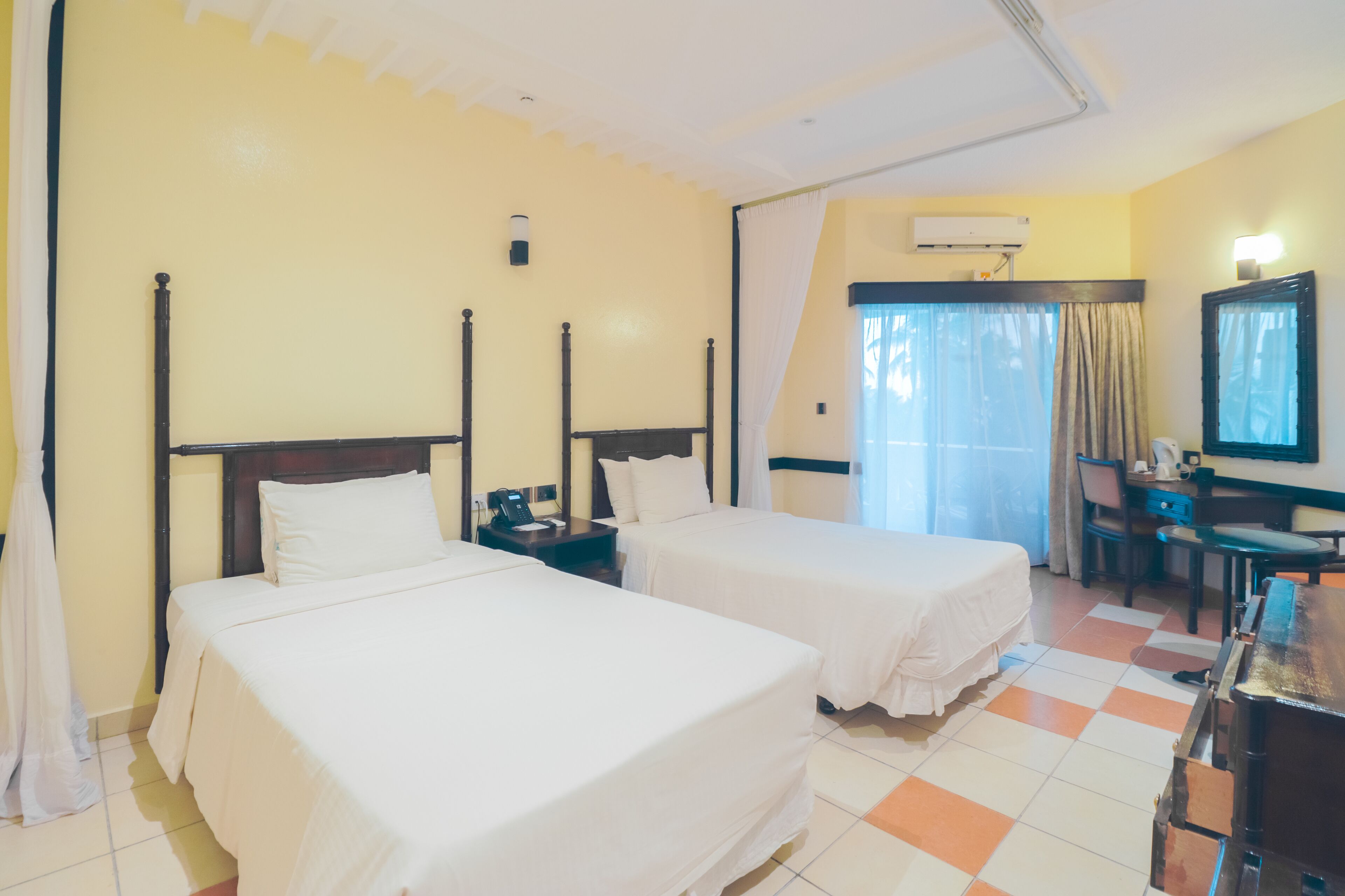 A hotel room with two single beds, a desk, a chair, an air conditioning unit, and a television.