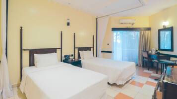 A hotel room with two single beds, a desk, a chair, an air conditioning unit, and a television.