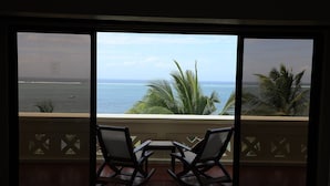 A balcony with two rocking chairs and a small table, overlooking a beach with palm trees and the ocean. - Mombasa Continental Resort (Mombasa)