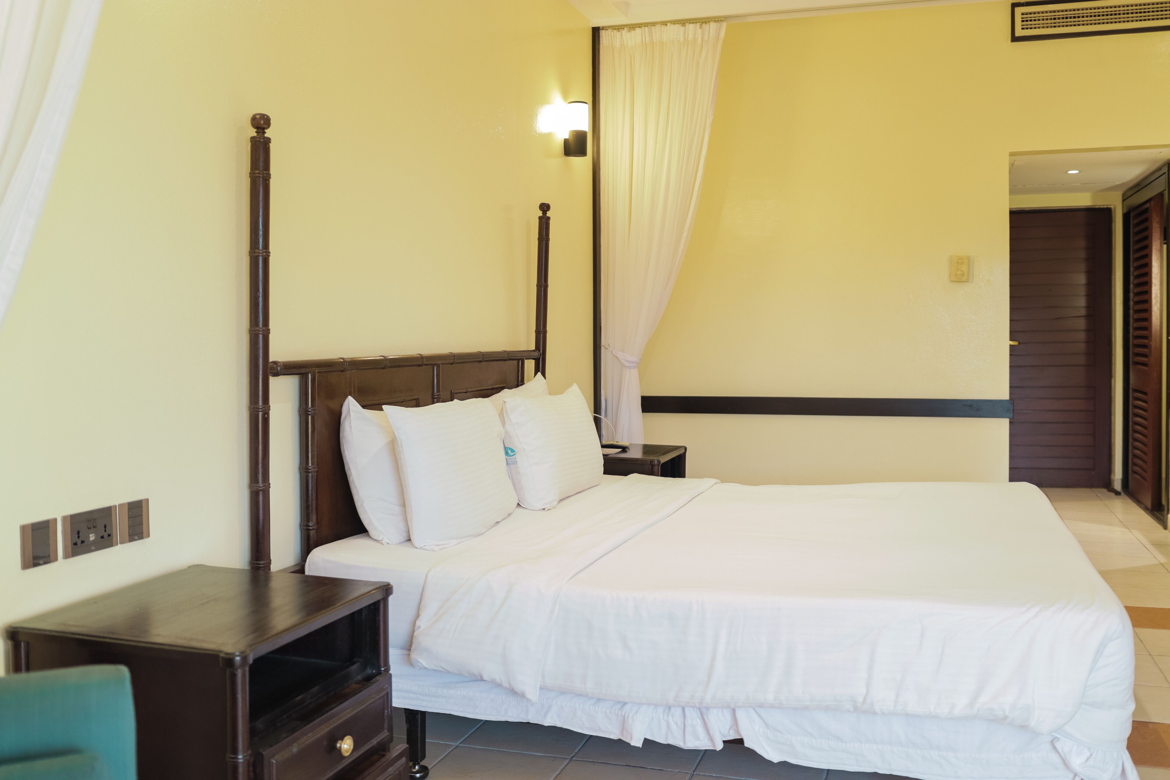 A neatly made bed with white linens, a wooden headboard, and a bedside table with a lamp.
