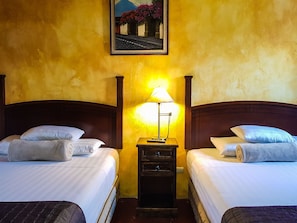 Una habitación de hotel con dos camas individuales, una mesita de noche con una lámpara y un cuadro en la pared.
