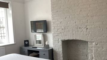 A bedroom with a large bed, a desk with a computer, a television, and a white brick fireplace.