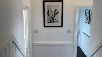 A hallway with white wainscoting, a framed floral artwork on the wall, and a carpeted floor.