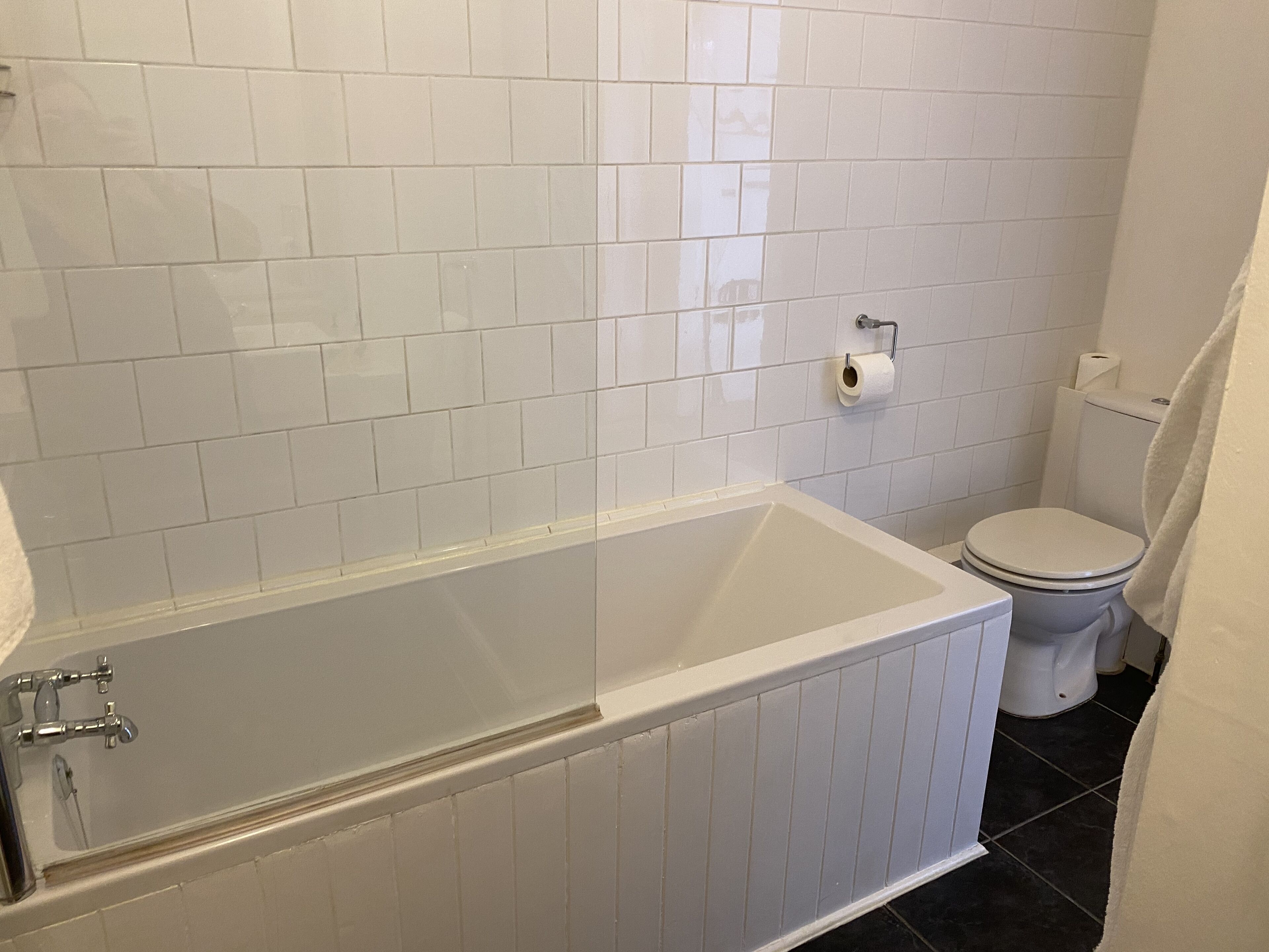 Et badeværelse med badekar, toilet og vægge beklædt med hvide fliser.
