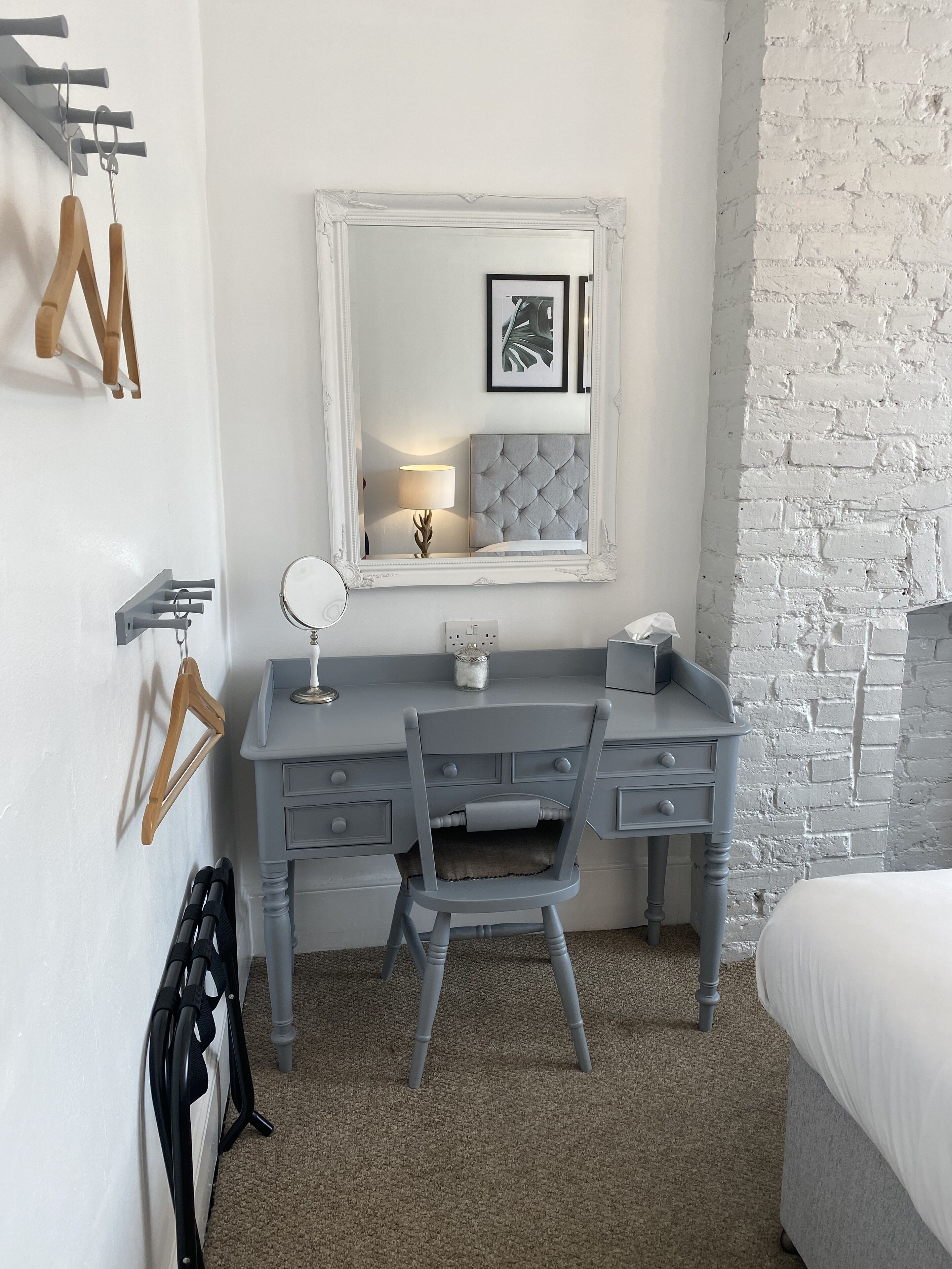 A bedroom with a grey dresser, a chair, a bed, a mirror, and a white brick wall.