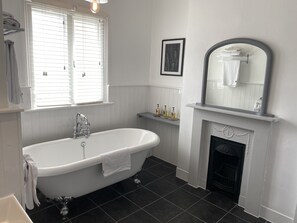 Une salle de bain avec une baignoire sur pieds, une cheminée et une fenêtre avec des stores.