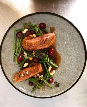 A plate with salmon, green beans, cherries, and pine nuts.
