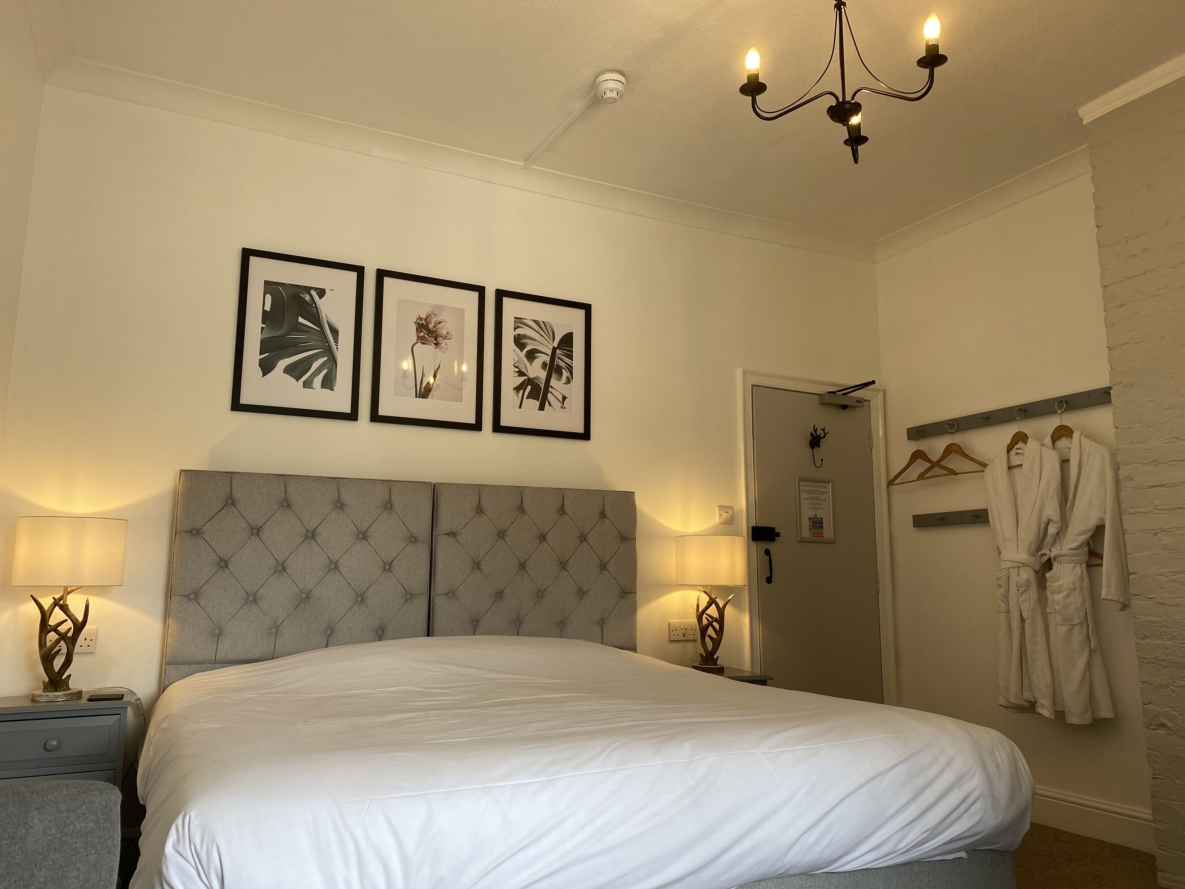 A neatly made bed with a tufted headboard, two bedside lamps, and framed botanical prints on the wall.