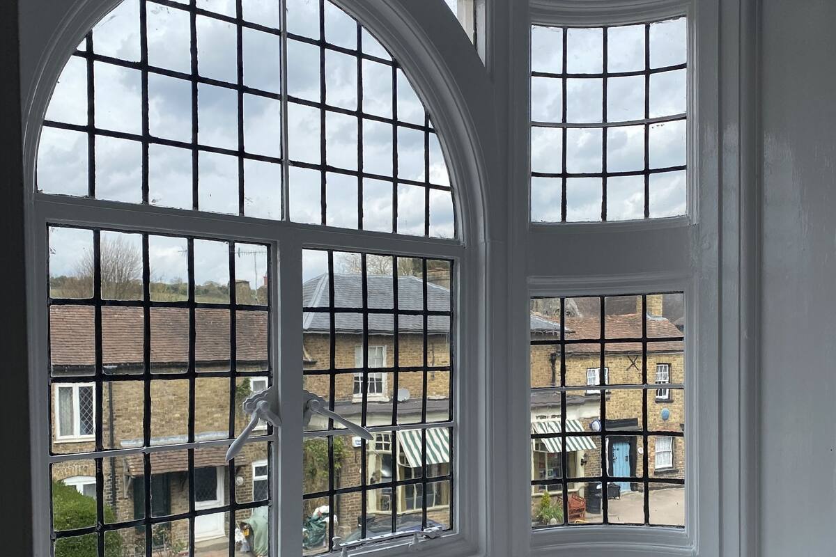 A room with large arched windows with multiple panes, a white ceiling, and a view of neighboring houses.