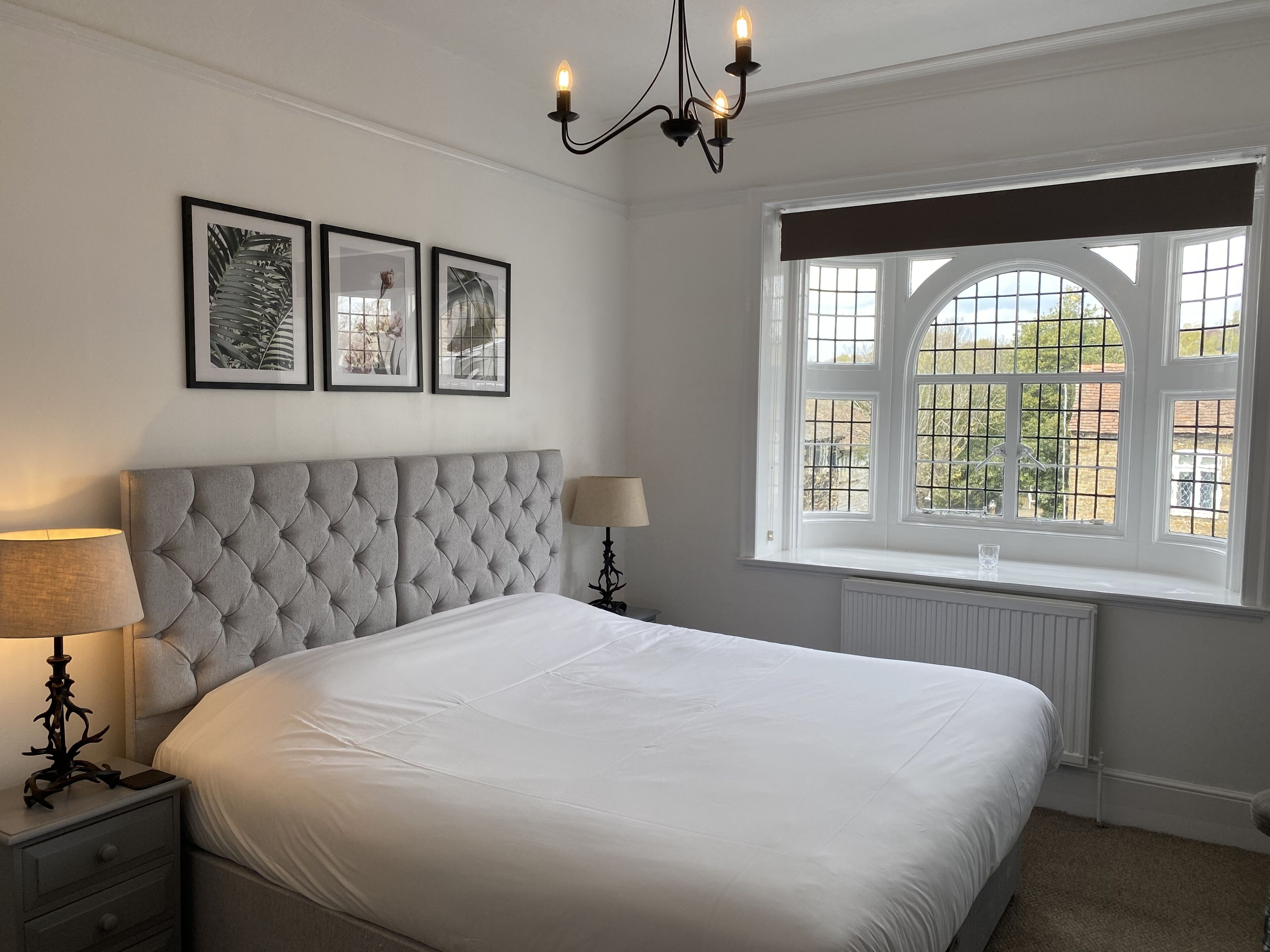 A bedroom with a tufted headboard, a large window with a view, and framed artwork on the wall.