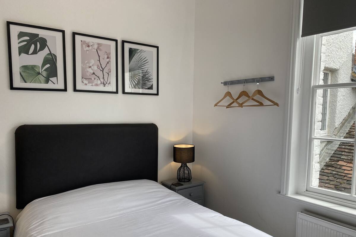 A neatly made bed with a black headboard, a bedside lamp, and three framed botanical prints on the wall.
