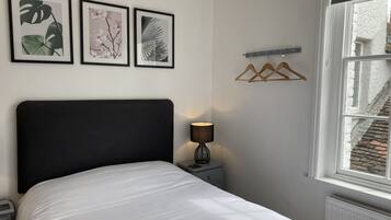 Ein ordentlich bezogenes Bett mit schwarzem Kopfteil, einer Nachttischlampe und drei gerahmten Pflanzenbildern an der Wand.