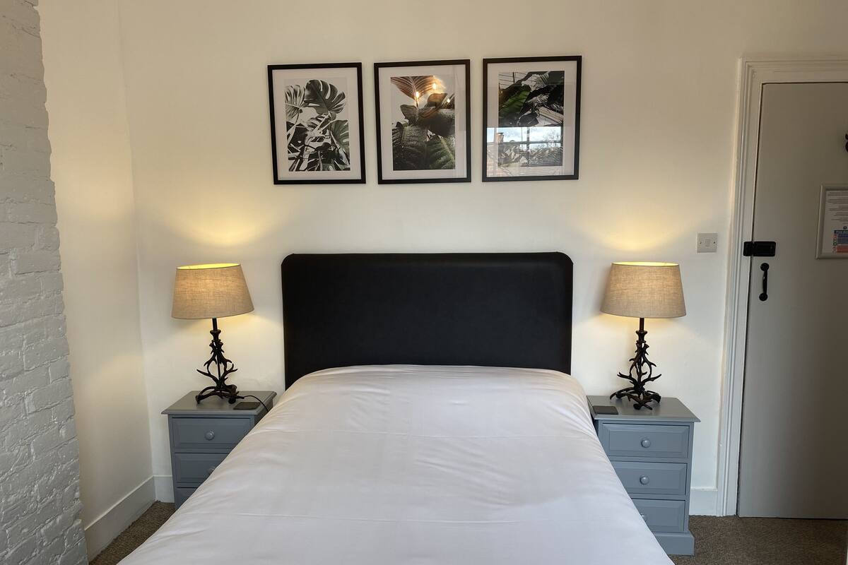 A neatly made bed with a black headboard, two bedside tables with lamps, and three framed botanical prints on the wall.