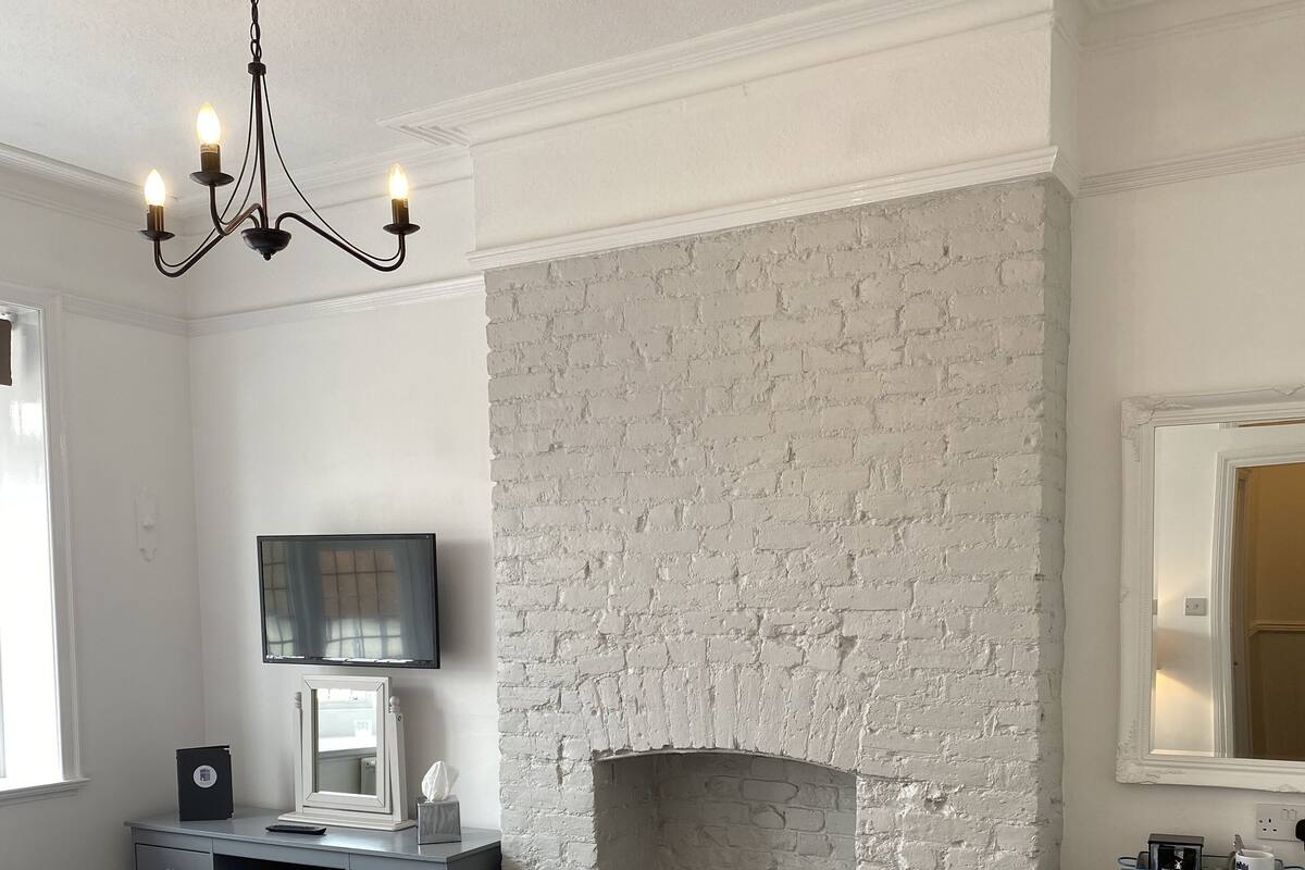 A bedroom with a large bed, a white brick fireplace, a desk with a computer, and a chair.