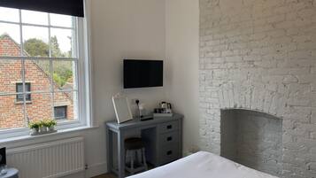 A bedroom with a large window, a desk, a chair, a bed, a flat-screen TV, and a fireplace.