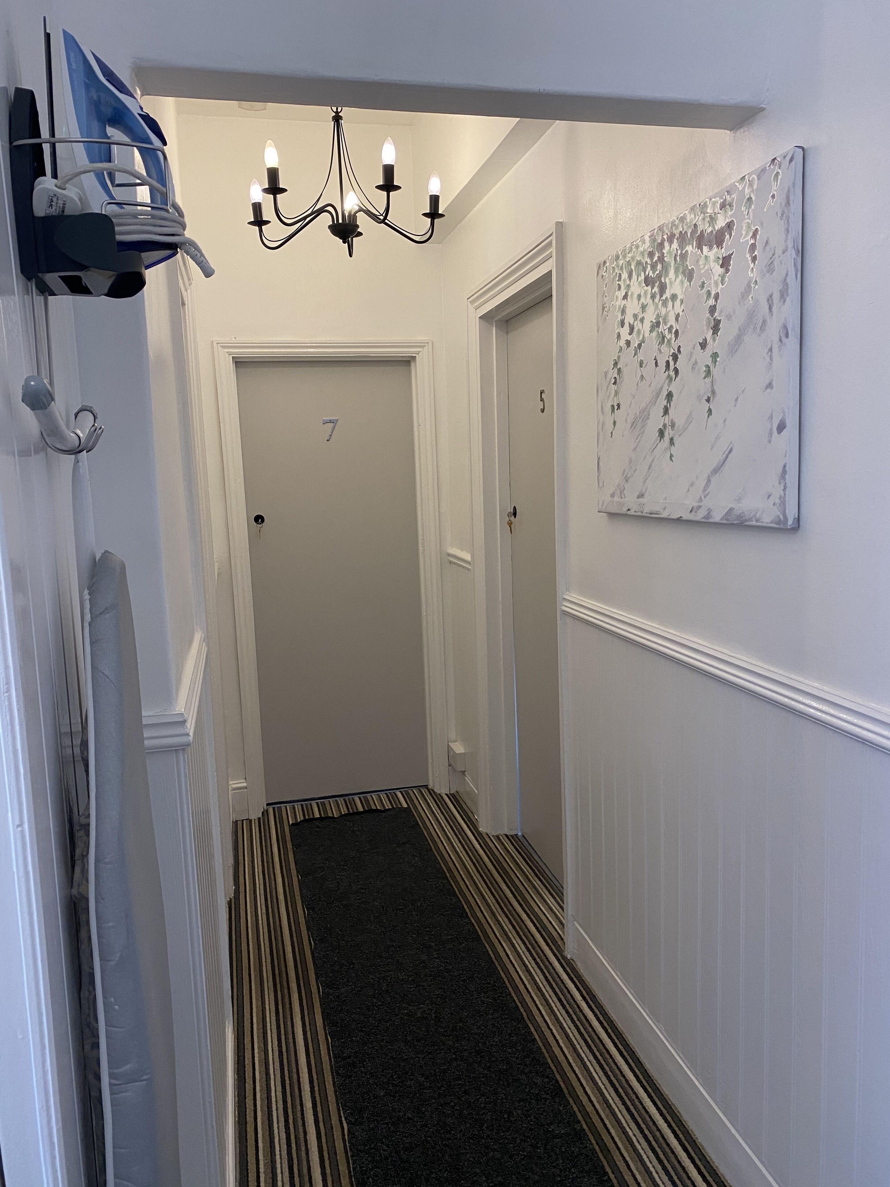 A hallway with a black and white striped carpet, a chandelier, and a painting on the wall.