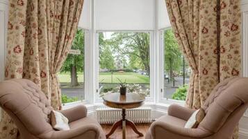 A room with two armchairs, a round table, and a view of a green landscape through large windows.