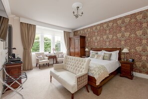 A bedroom with a large bed, a sitting area with a sofa, a wooden wardrobe, and a desk with a chair.