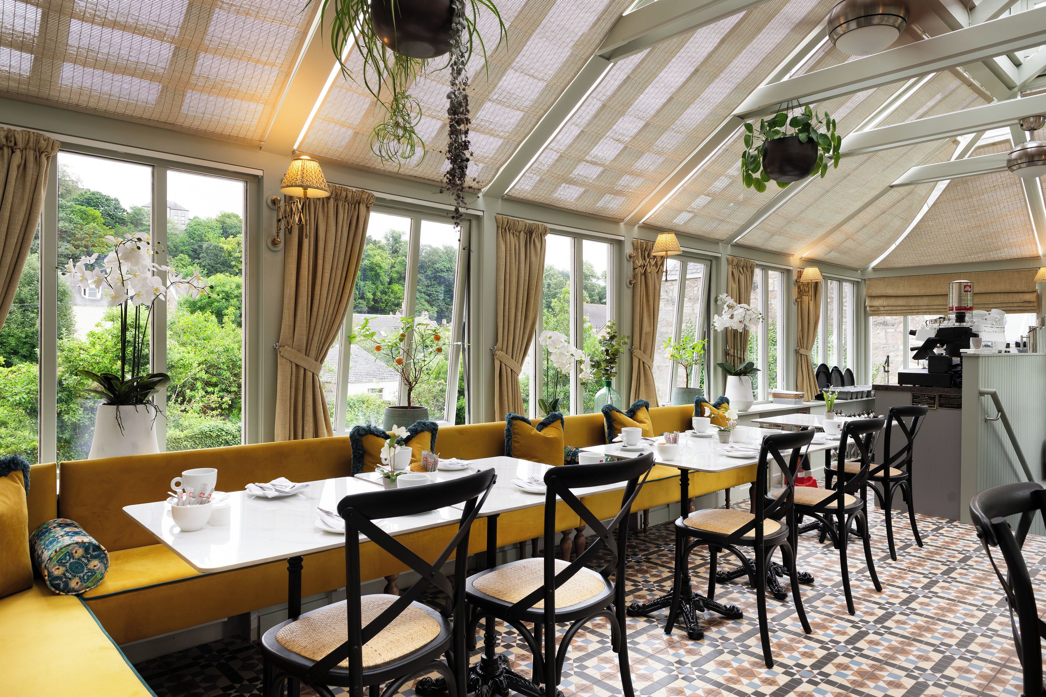 A restaurant with a long dining table, chairs, and a view of greenery outside.