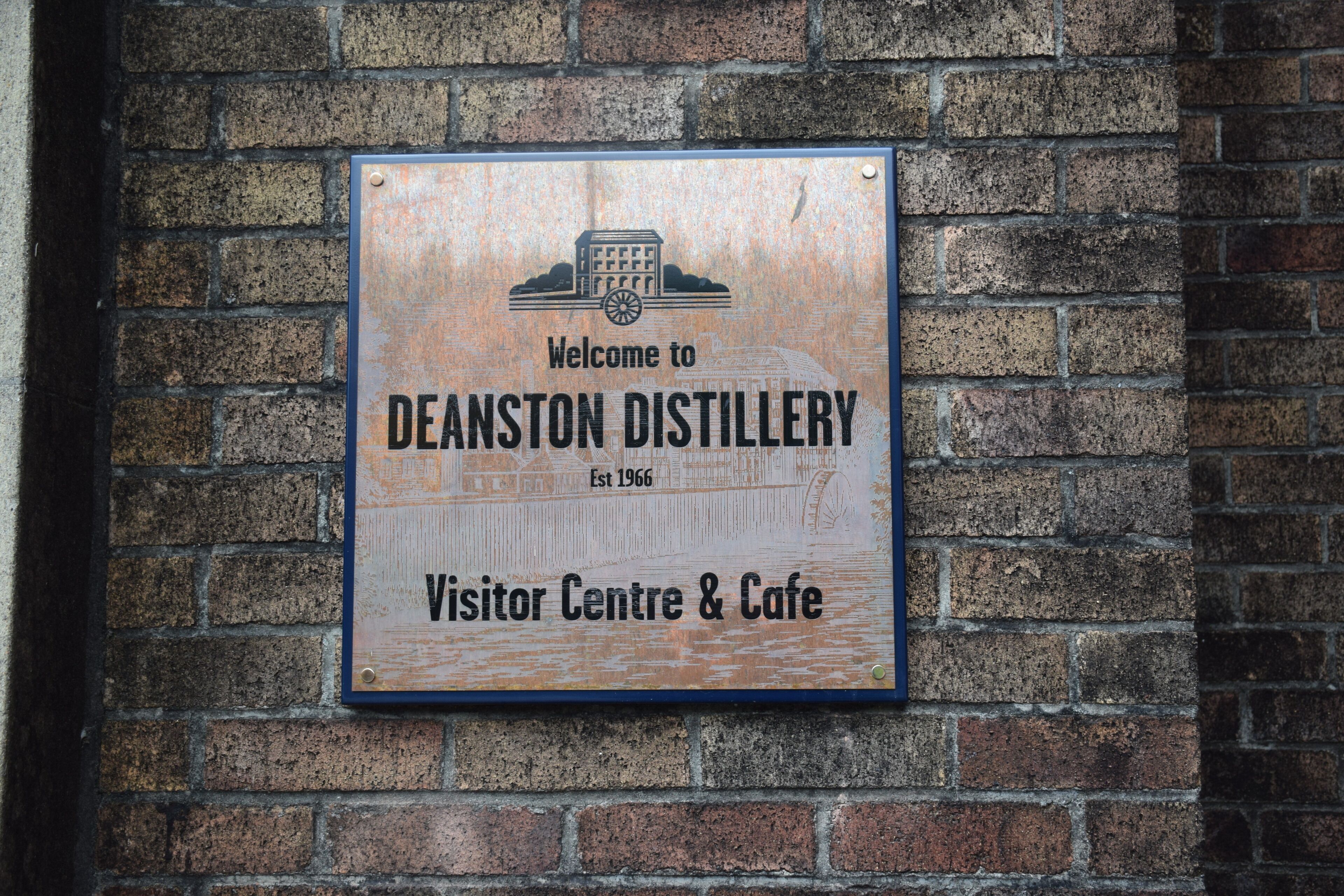 Placa da Deanston Distillery, indicando que é um centro de visitantes e café.