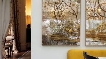 A room with a yellow sofa, a patterned rug, a vase, and two large paintings on the wall.