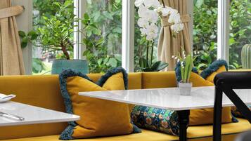 Un canapé jaune, une table blanche et une plante devant une fenêtre donnant sur un paysage verdoyant.