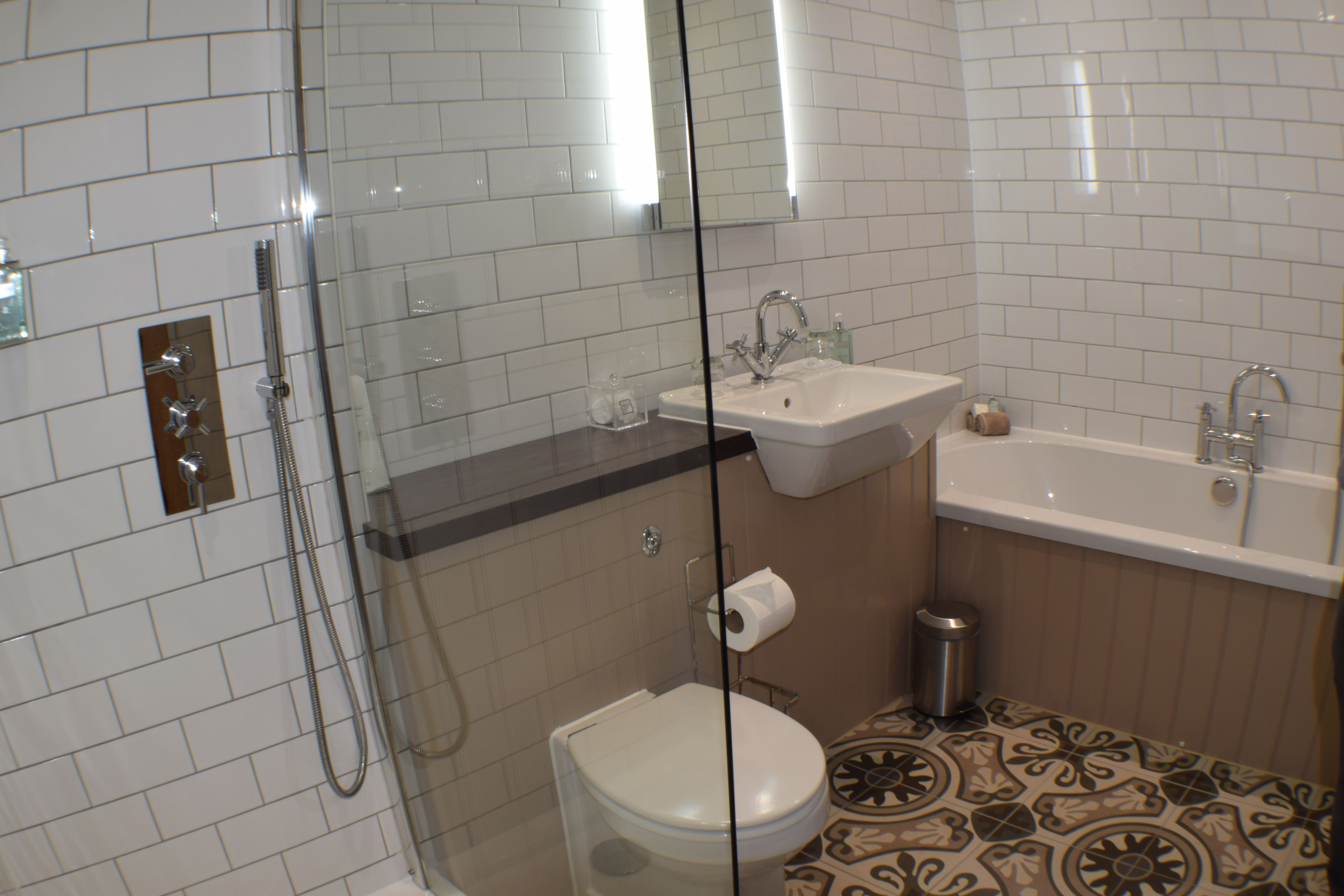 A bathroom with white tiled walls, a glass shower enclosure, a sink, and a toilet.