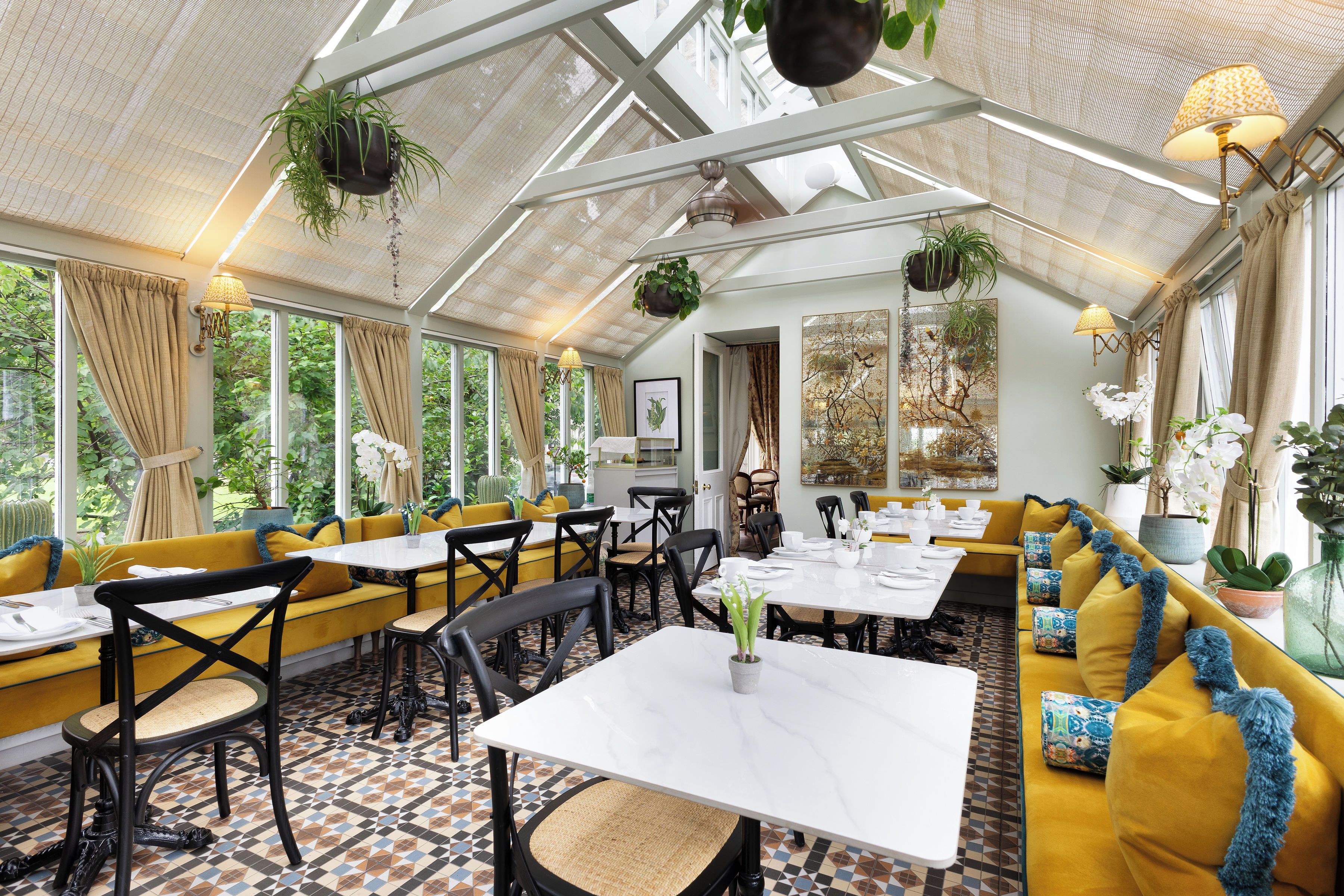 A conservatory with yellow sofas, black chairs, and a tiled floor.