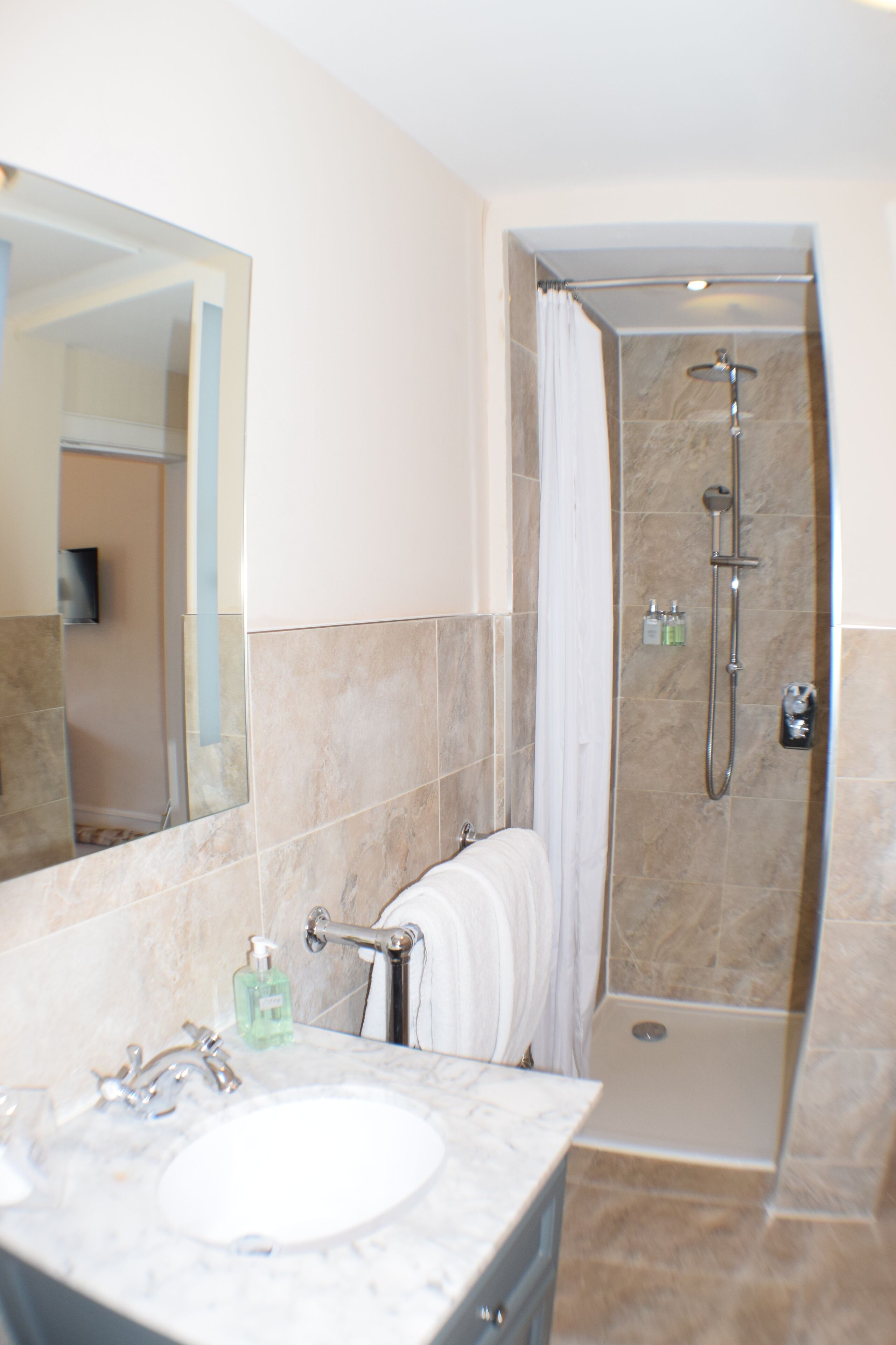 Un baño con lavamanos de mármol, un espejo grande, ducha con puerta de cristal y un perchero para toallas.