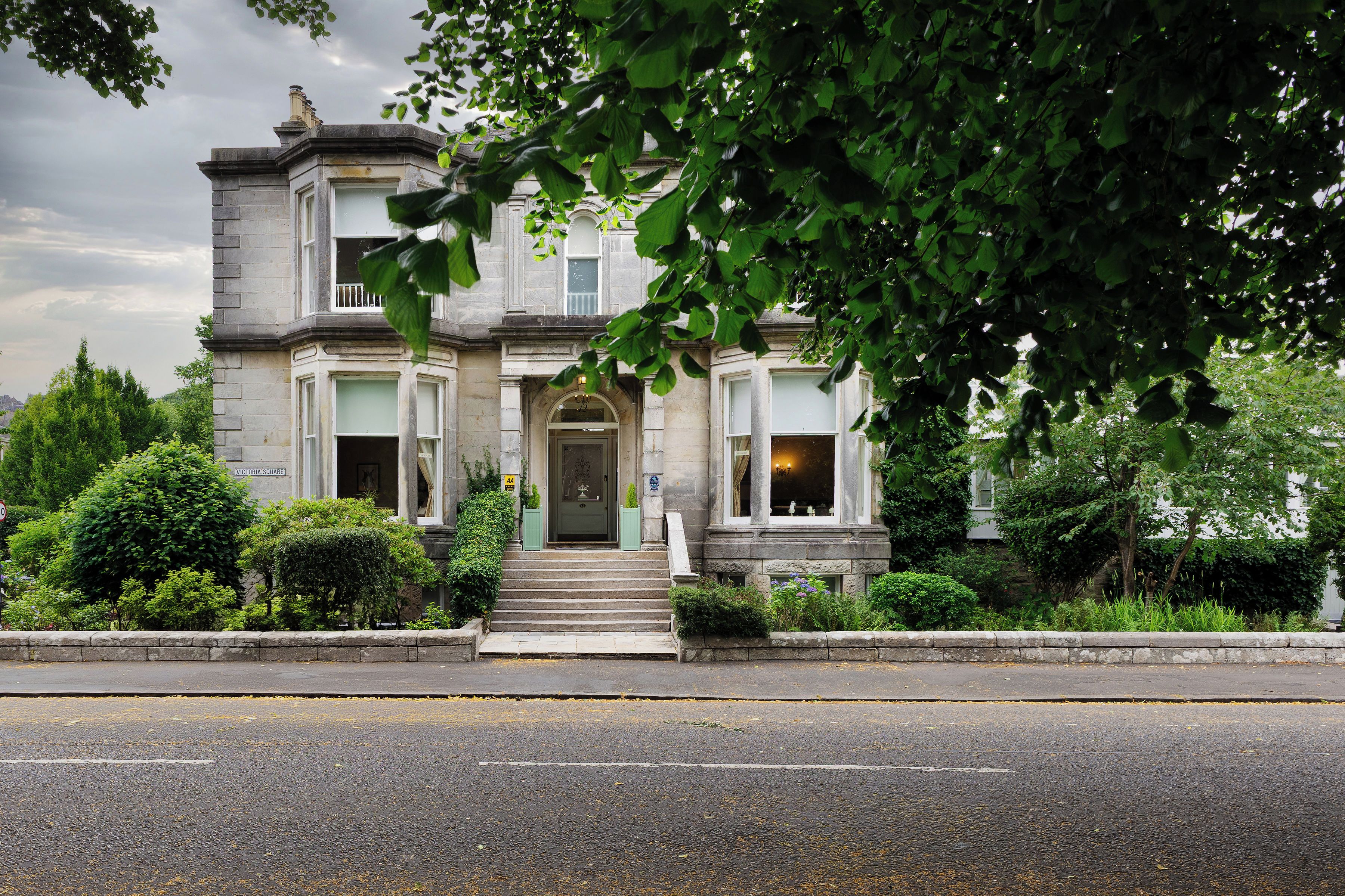 A historic building with a symmetrical facade, a central entrance with steps, and a well-maintained garden.