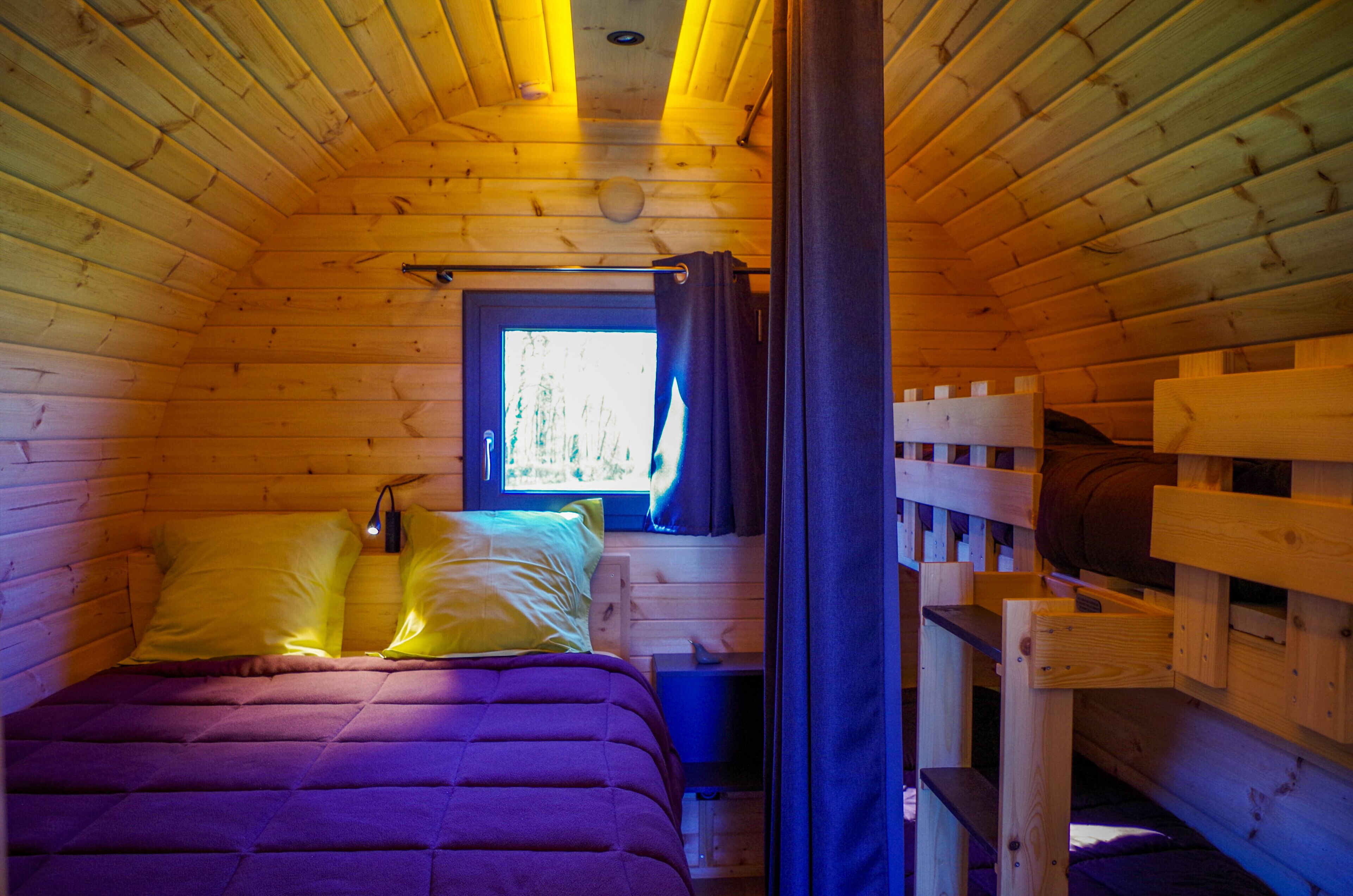 Una habitación tipo cabaña de madera con una cama, un ventanal con cortinas y una litera.