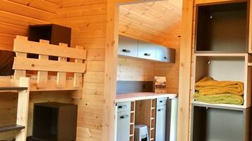 A cozy wooden cabin interior with a bed, built-in storage, and a kitchenette.