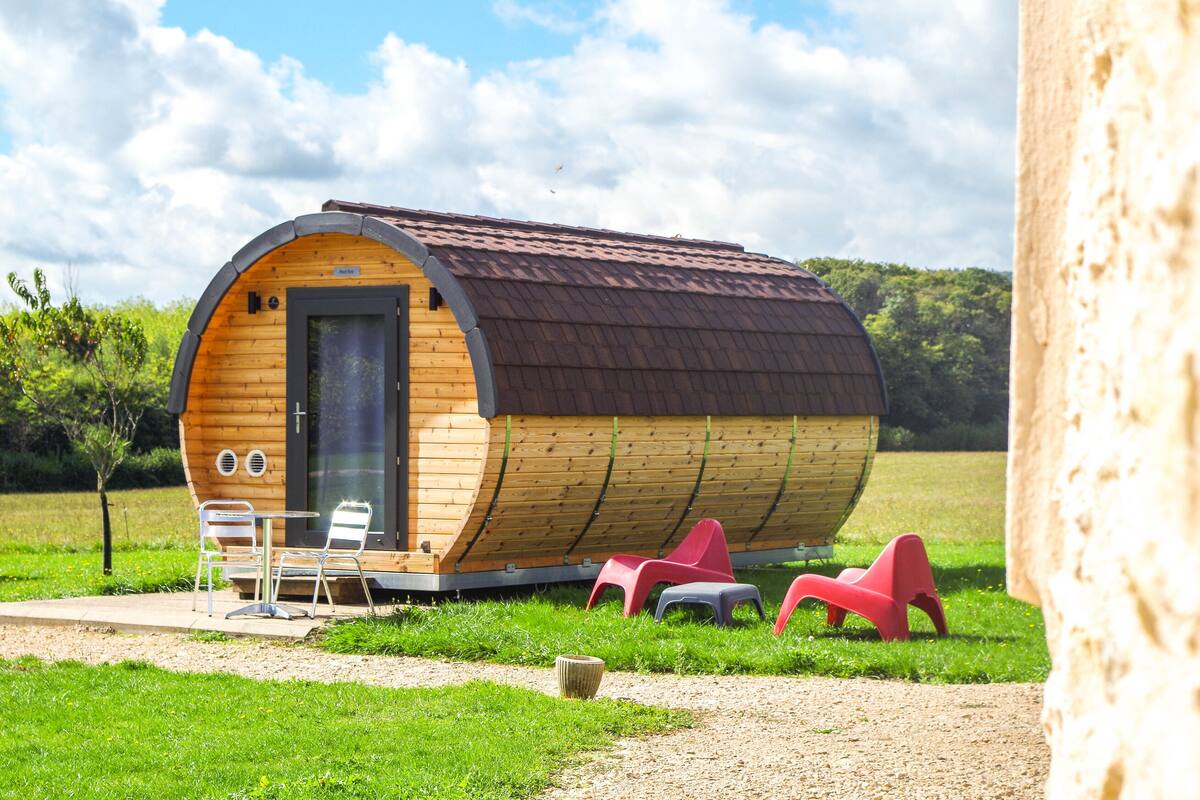 A wooden, barrel-shaped cabin with a door, windows, and a small patio area with chairs.